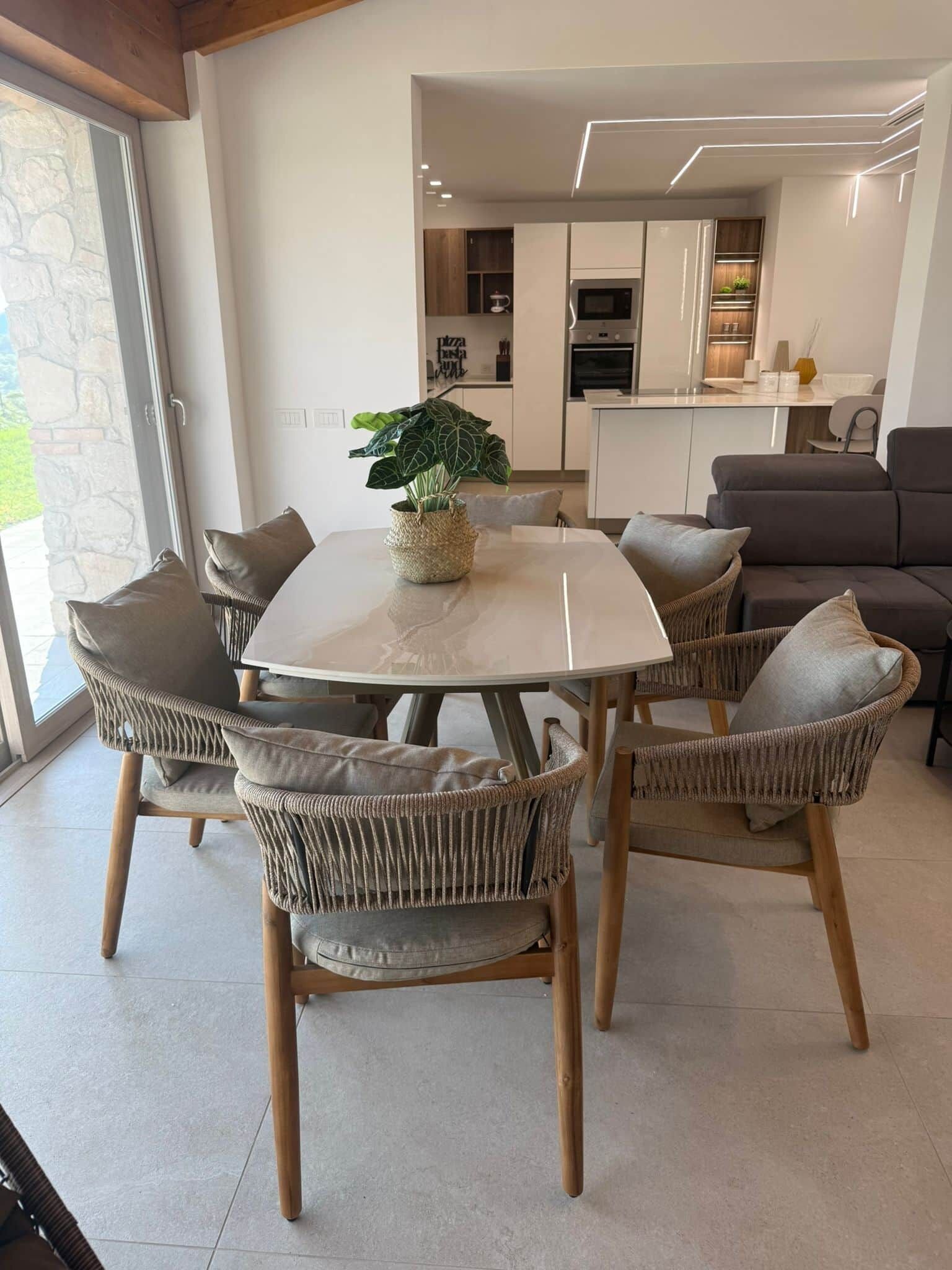 A modern dining area with a round table, wicker chairs, and a potted plant.