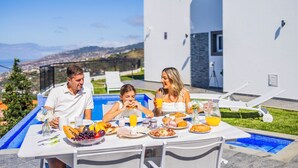 A family dining at a poolside table with a view of the city and mountains. - Zen House By The Madeira Luxury Collection (Arco da Calheta)