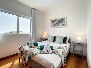 Ein Hotelzimmer mit einem großen Bett, zwei Nachttischen, einer Weltkarte als Kunstwerk und einem Fenster mit Blick.