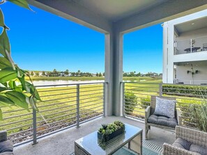 A balcony with a view of a golf course, a white building, and outdoor furniture. - Storey Lake Cozy 3BR Condo, Lake View, By Disney (Kissimmee)