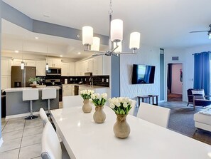 A modern kitchen with white cabinets, a central island, and a dining area with a white table and bar stools. - Storey Lake Cozy 3BR Condo, Lake View, By Disney (Kissimmee)