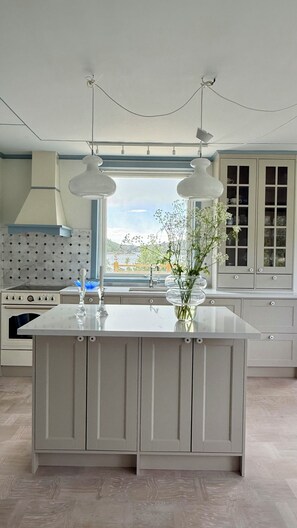 A modern kitchen with a central island, pendant lights, a view of the outdoors, and a built-in oven. - Villa Erik - A newly renovated summer oasis with sea views, peace and exclusive comfort. (Eriksberg)
