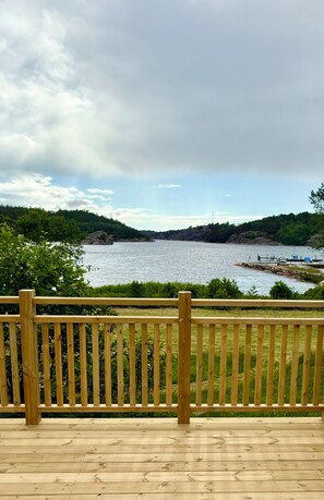Eine Holzterrasse mit Blick auf ein Gewässer, eine felsige Küstenlinie und viel Grün im Hintergrund.