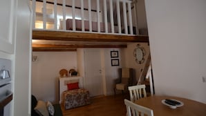 Ein Loft-Zimmer mit Holzboden, einem Esstisch, einem Stuhl, einer Couch, einem kleinen Tisch mit Dekoration und einer Tür sowie einer Treppe zu einer erhöhten Ebene.