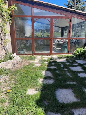 Ein Wintergarten mit Glastür, ein Garten mit trittfesten Steinen und Blick ins Freie.