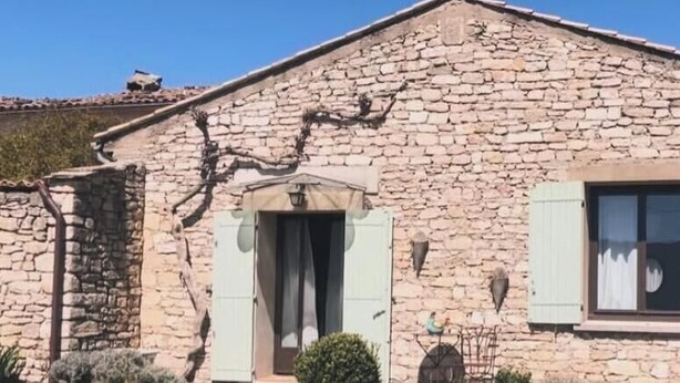 Un bâtiment en pierre avec un toit à deux versants, une porte et deux fenêtres dotées de volets.