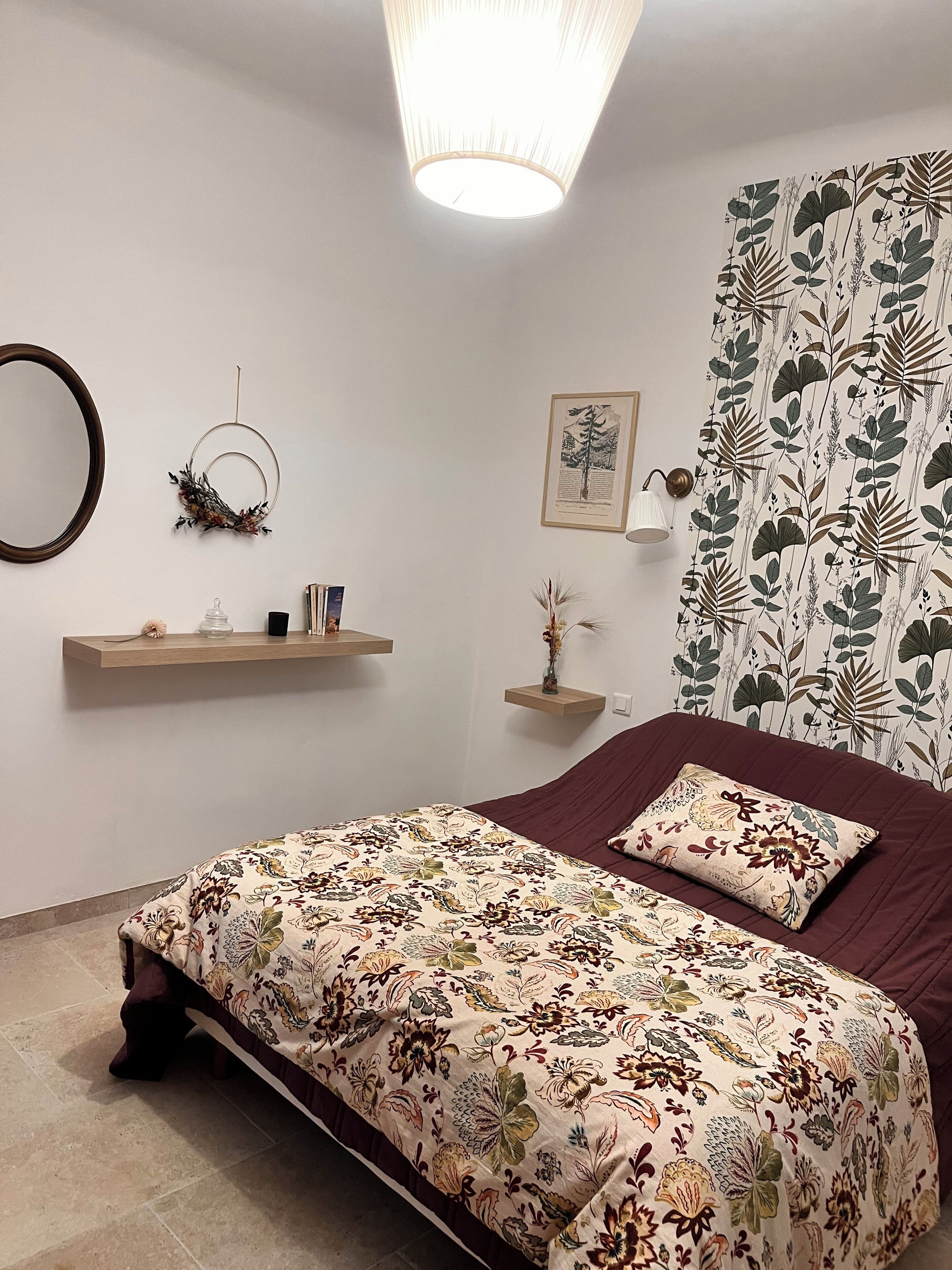 A bedroom with a bed, a wall-mounted shelf, a framed picture, and a patterned curtain.