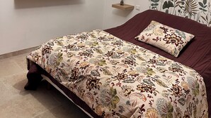 Une chambre à coucher avec un lit, une étagère fixée au mur, un tableau encadré et un rideau à motifs.