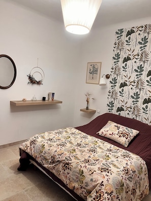 Ein Schlafzimmer mit einem Bett, einem an der Wand befestigten Regal, einem gerahmten Bild und einem gemusterten Vorhang.