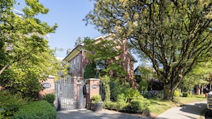 A brick building with a gated entrance, a paved driveway, and surrounding greenery. - Central 3BR Townhouse  Near Oakridge & SkyTrain to Airport & BC Place (Vancouver)