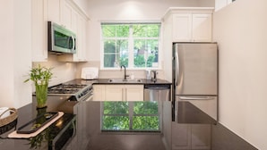 A modern kitchen with a stove, sink, and refrigerator, a window with a view of greenery, and white cabinetry. - Central 3BR Townhouse  Near Oakridge & SkyTrain to Airport & BC Place (Vancouver)