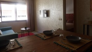 Ein Essbereich mit einem Holztisch, gedeckt für zwei Personen, einem an der Wand montierten Fernseher und einem Fenster mit Vorhängen.
