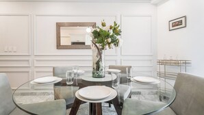 En spiseplads med et glasbord, hvide tallerkener og en vase med blomster.
