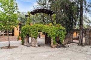 Un espacio de estar al aire libre cubierto, con pilares de piedra, plantas en macetas y una lámpara colgante.