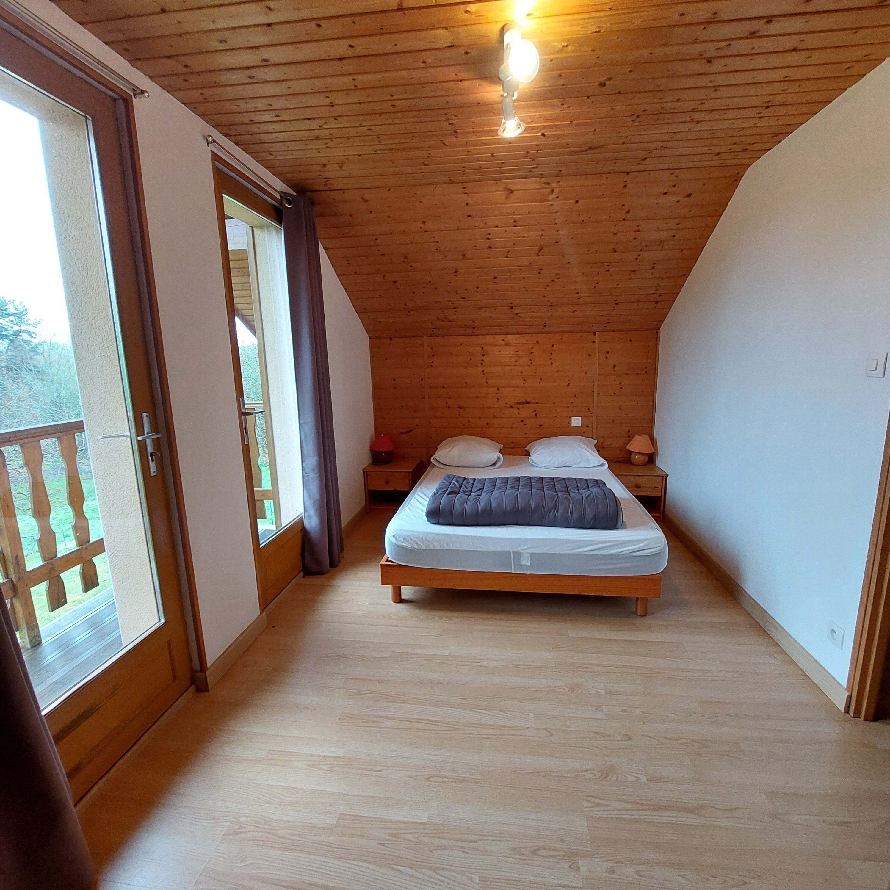 A bedroom with a wooden ceiling, a bed with pillows, a nightstand, and a window with curtains.