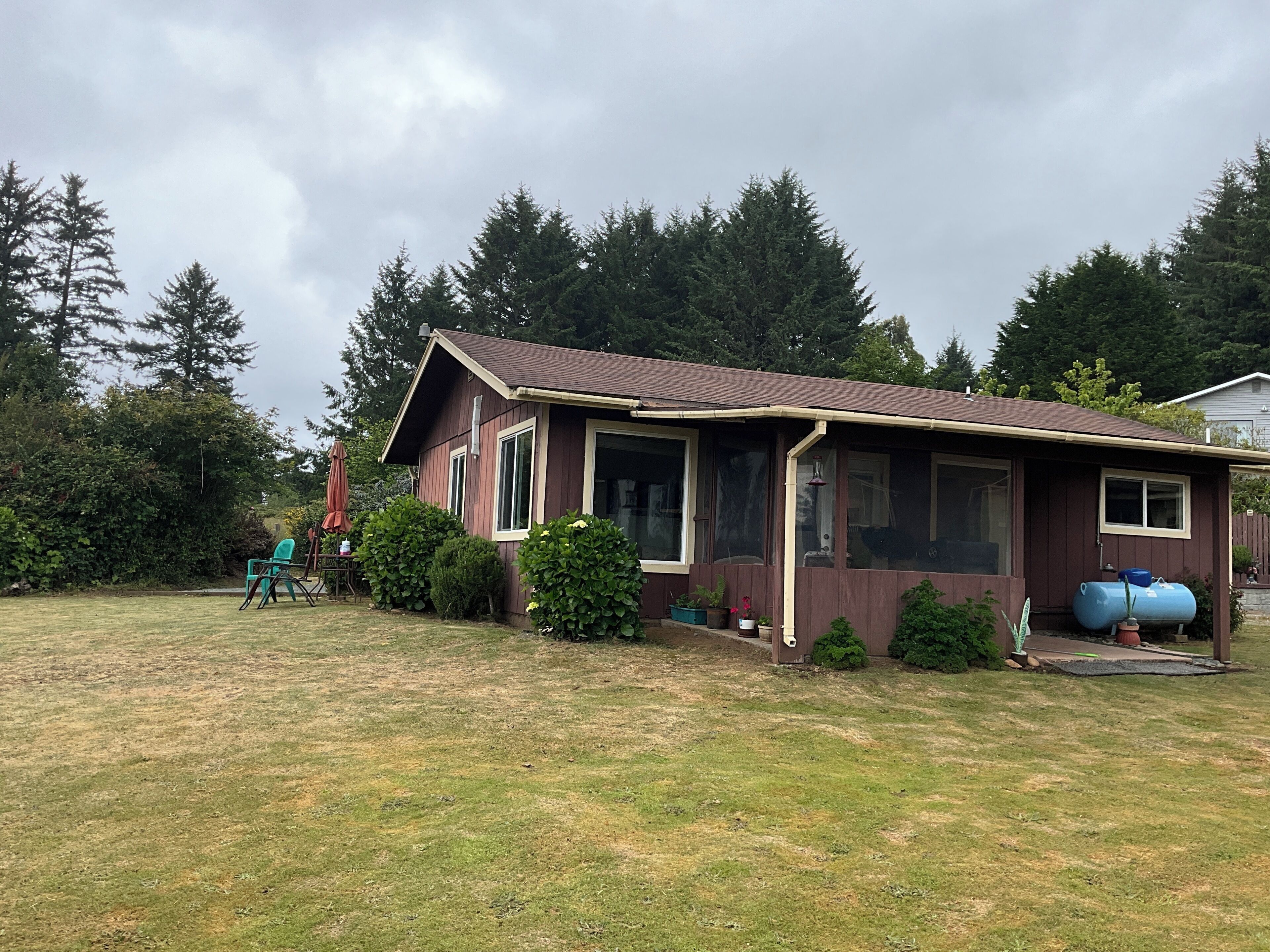 A single-story house with a front porch, a covered patio, and a yard with a lawn and shrubs.