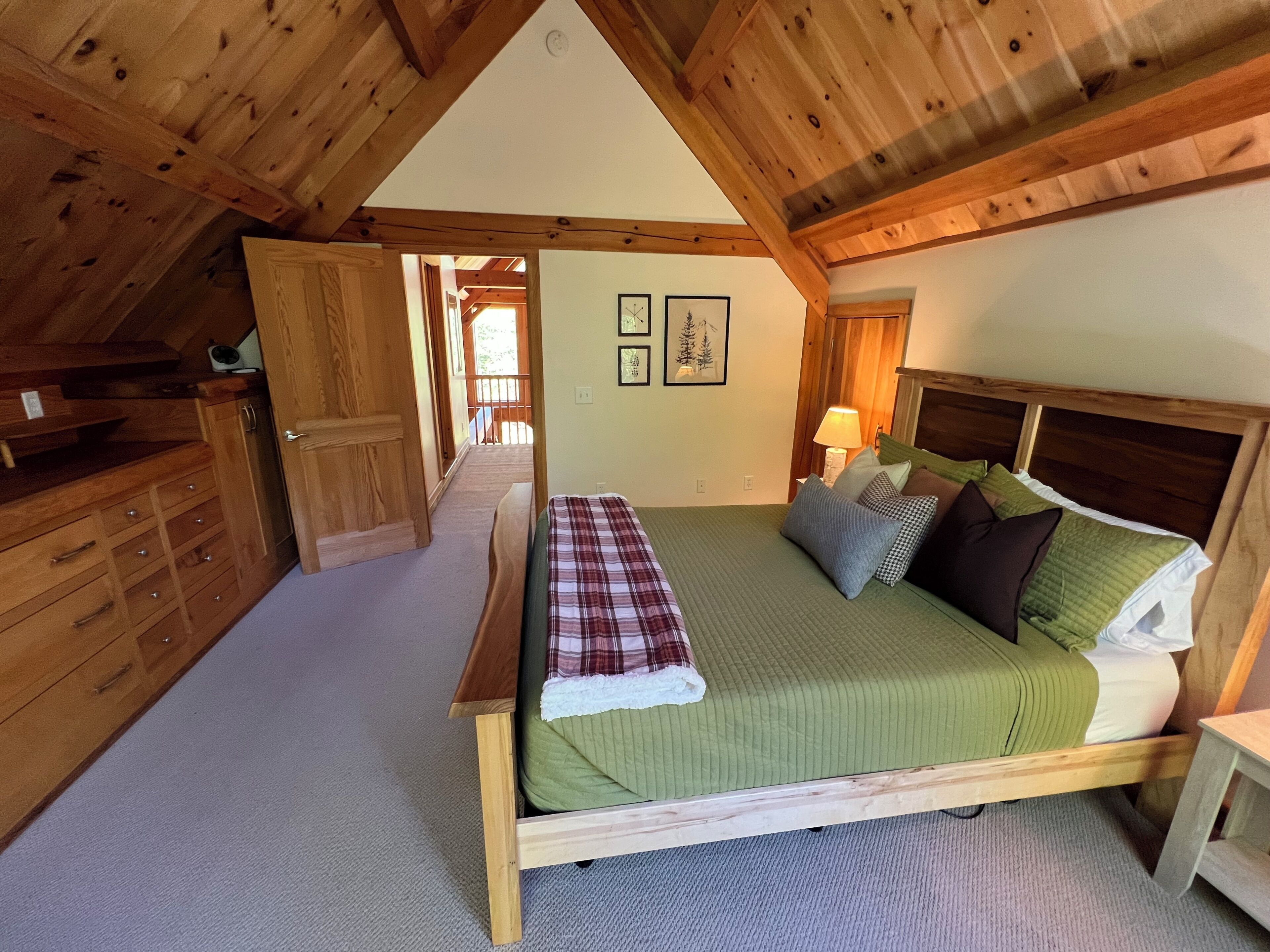 Camera da letto con struttura in legno, un letto, una cassettiera e una porta che dà su un'altra stanza.