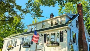 Ein zweistöckiges Haus mit Veranda, Schornstein und einer amerikanischen Flagge.