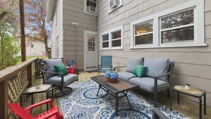 A covered patio with outdoor furniture, a patterned rug, and a view of a house with multiple windows. - Historic Gem in the Heart of Littleton (Littleton)