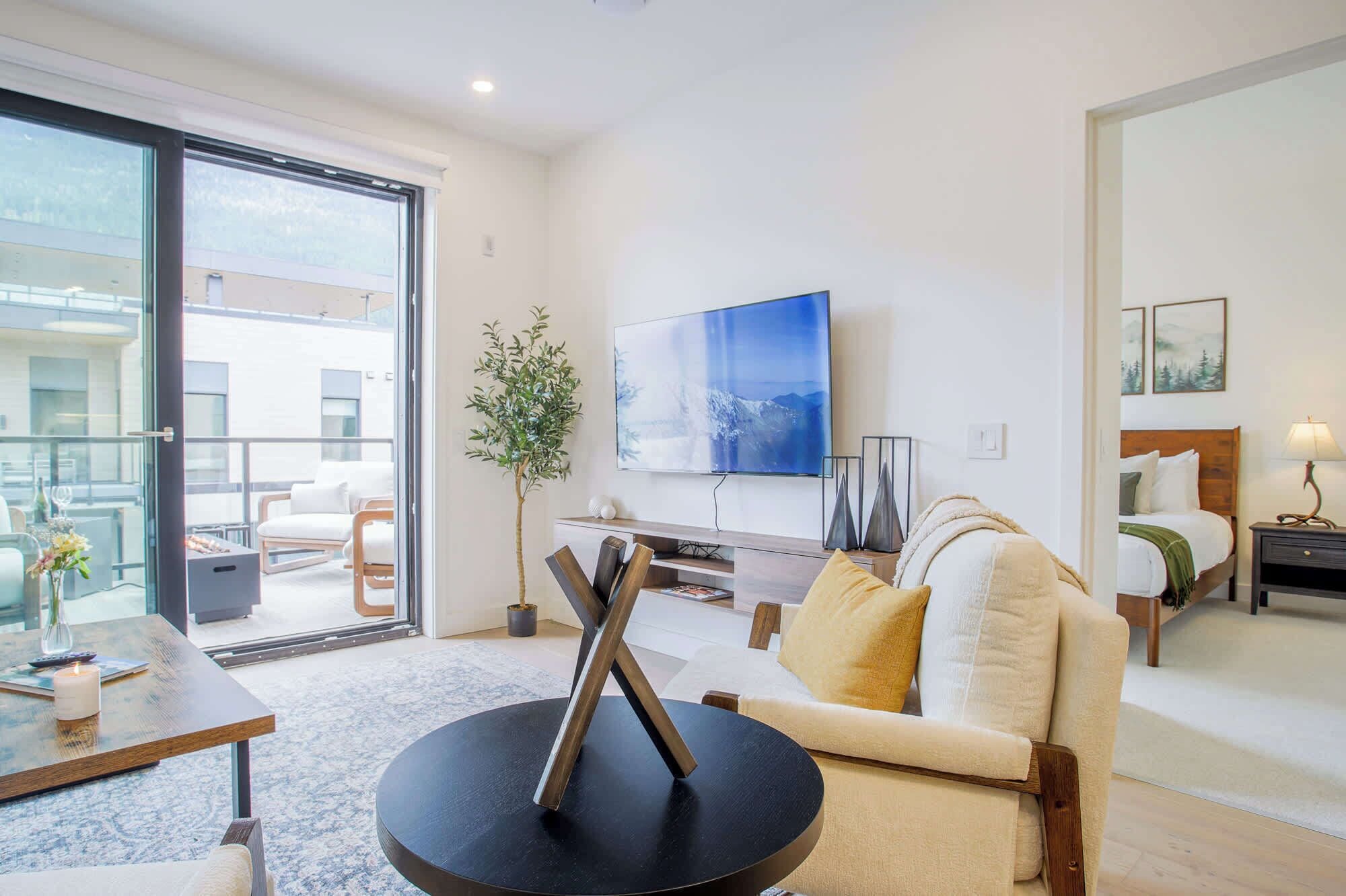 A modern living room with a sofa, a coffee table, a TV, and a balcony with outdoor furniture.