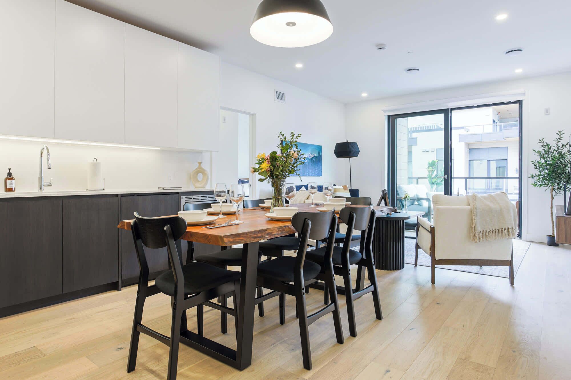 A modern kitchen with a dining area, wooden flooring, and large windows.