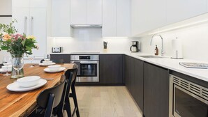 Cozinha moderna com armários brancos, forno Bosch, cafeteira e área de jantar com mesa e cadeiras de madeira.