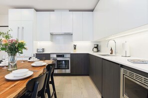 Eine moderne Küche mit weißen Schränken, einem Bosch-Ofen, einer Kaffeemaschine und einem Essbereich mit einem Holztisch und Stühlen.
