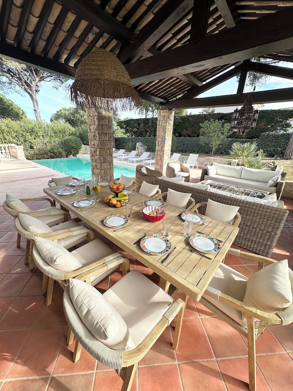 An outdoor dining area with a pool view, wicker furniture, and a thatched roof. - Villa Golf Esterel 150m2 quiet with swimming pool (Saint-Raphaël)