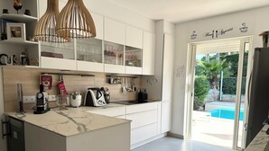 A modern kitchen with a marble countertop, a built-in oven, and a glass door leading to a pool. - Villa Golf Esterel 150m2 quiet with swimming pool (Saint-Raphaël)