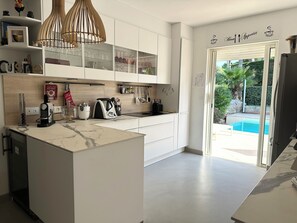 A modern kitchen with a marble countertop, a built-in oven, and a glass door leading to a pool. - Villa Golf Esterel 150m2 quiet with swimming pool (Saint-Raphaël)
