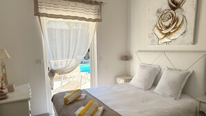A neatly made bed with white and brown linens, a bedside table with a lamp, and a painting of roses on the wall. - Villa Golf Esterel 150m2 quiet with swimming pool (Saint-Raphaël)
