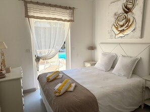 A neatly made bed with white and brown linens, a bedside table with a lamp, and a painting of roses on the wall. - Villa Golf Esterel 150m2 quiet with swimming pool (Saint-Raphaël)