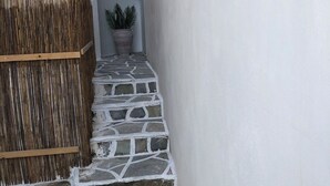 A narrow stone pathway leading to a door, with a bamboo fence on one side and a potted plant on the other. - Celia amazing view at the port of Adamas (Adamantas)