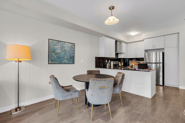 Een moderne keuken met witte kasten, een roestvrijstalen koelkast en een eethoek met een ronde tafel en stoelen.