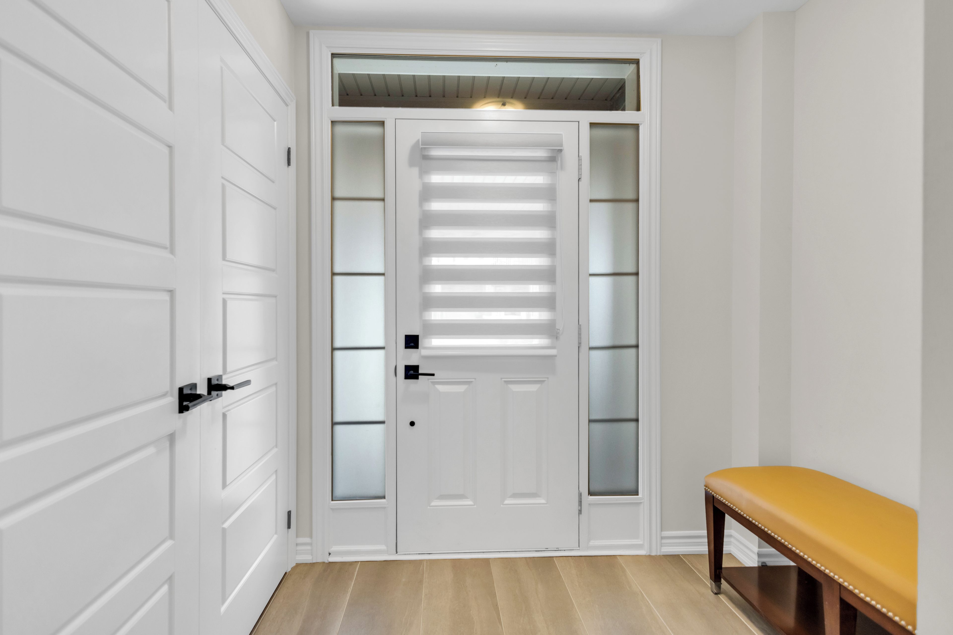 A hallway with a white door, a bench, and a light fixture above the door.