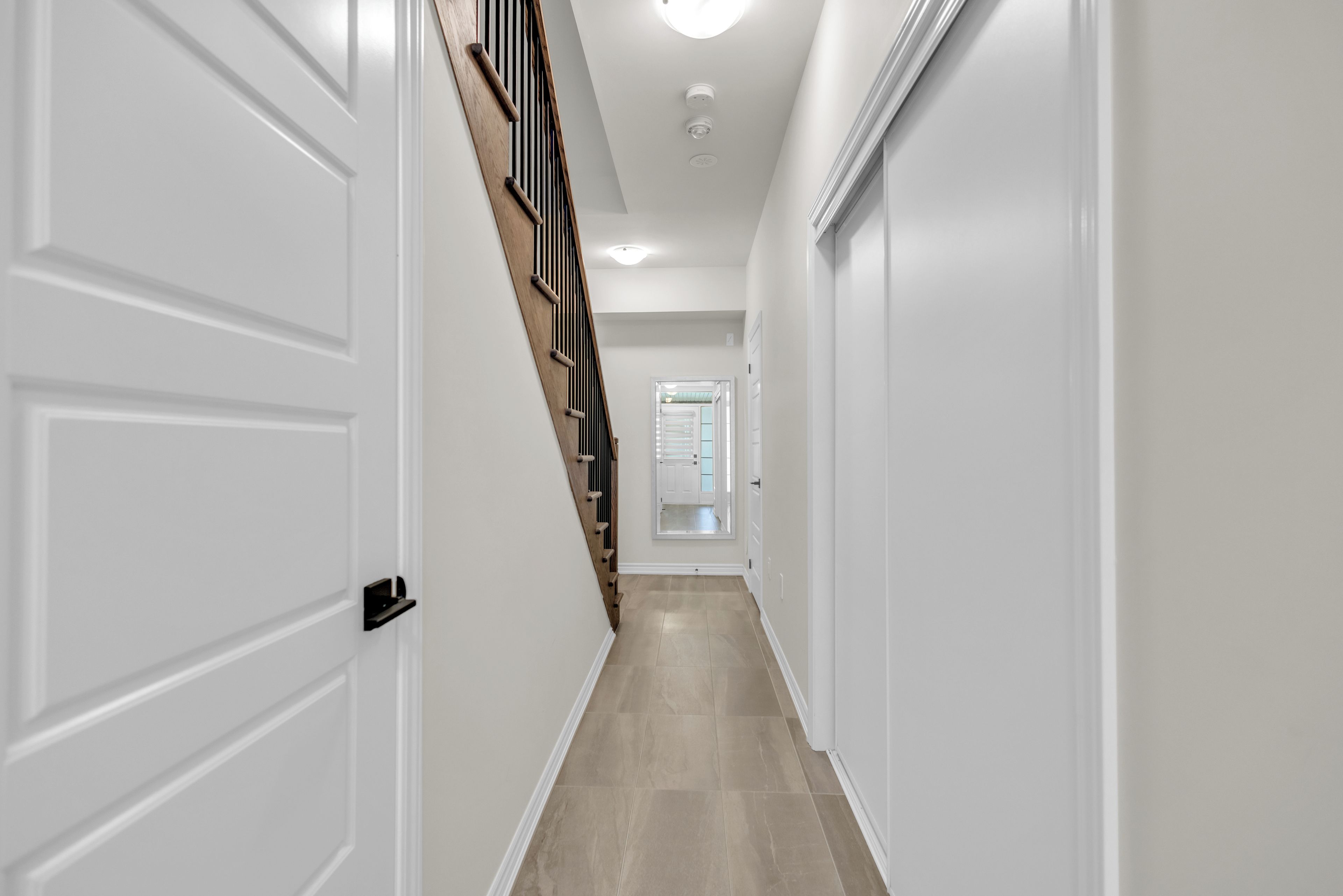 Un couloir avec des portes blanches, un escalier en bois et une vue sur une pièce dotée d’une fenêtre.