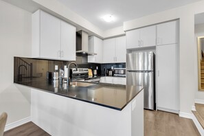 A modern kitchen with white cabinetry, stainless steel appliances, and a black countertop.