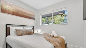 Een slaapkamer met een bed, een raam met uitzicht op bomen, een schilderij aan de muur en een plafondlamp.