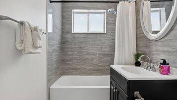 Un baño moderno con bañera, ducha, tocador con lavamanos y espejo.