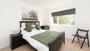Een slaapkamer met een bed, nachtkastjes, een stoel, een raam en een schilderij aan de muur.