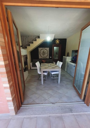 A dining area with a table and chairs, a staircase, a clock, and a television. - La Rosa dei Venti (Nebida)