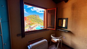Uma casa de banho com janela vista para uma piscina e edifícios, um radiador e uma pequena estante com espelho.