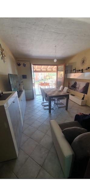 A compact living space with a kitchen, dining area, and a view to an outdoor patio. - La Rosa dei Venti (Nebida)