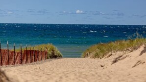 En sti langs stranden der fører ned til havet, med sand og græs på begge sider.