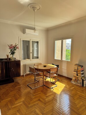 Ein Essbereich mit Holztisch und -stühlen, einem Heizkörper, einem Fenster mit Blick und einem Stapel Bücher.