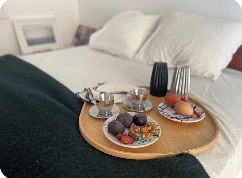 Un lit recouvert de draps blancs, une table de chevet sur laquelle se trouve un plateau avec des assiettes de nourriture, une tasse et une fourchette.