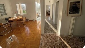 A spacious room with a wooden floor, a round table with chairs, and a large window. - Quiet Designer Home, 2BR, Sunset Balcony • Kypseli (Athina)