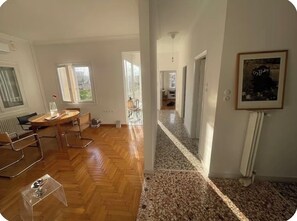 Ein geräumiges Zimmer mit Holzboden, einem runden Tisch mit Stühlen und einem großen Fenster.