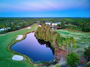 A golf course with a pond, trees, and a large building in the background.