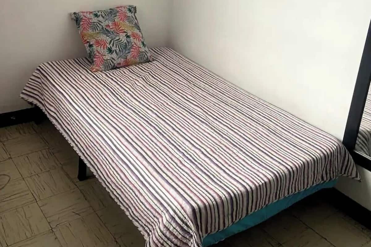 Ein kleines Zimmer mit einem Einzelbett, einer gestreiften Bettdecke und einem farbenfrohen Kissen.